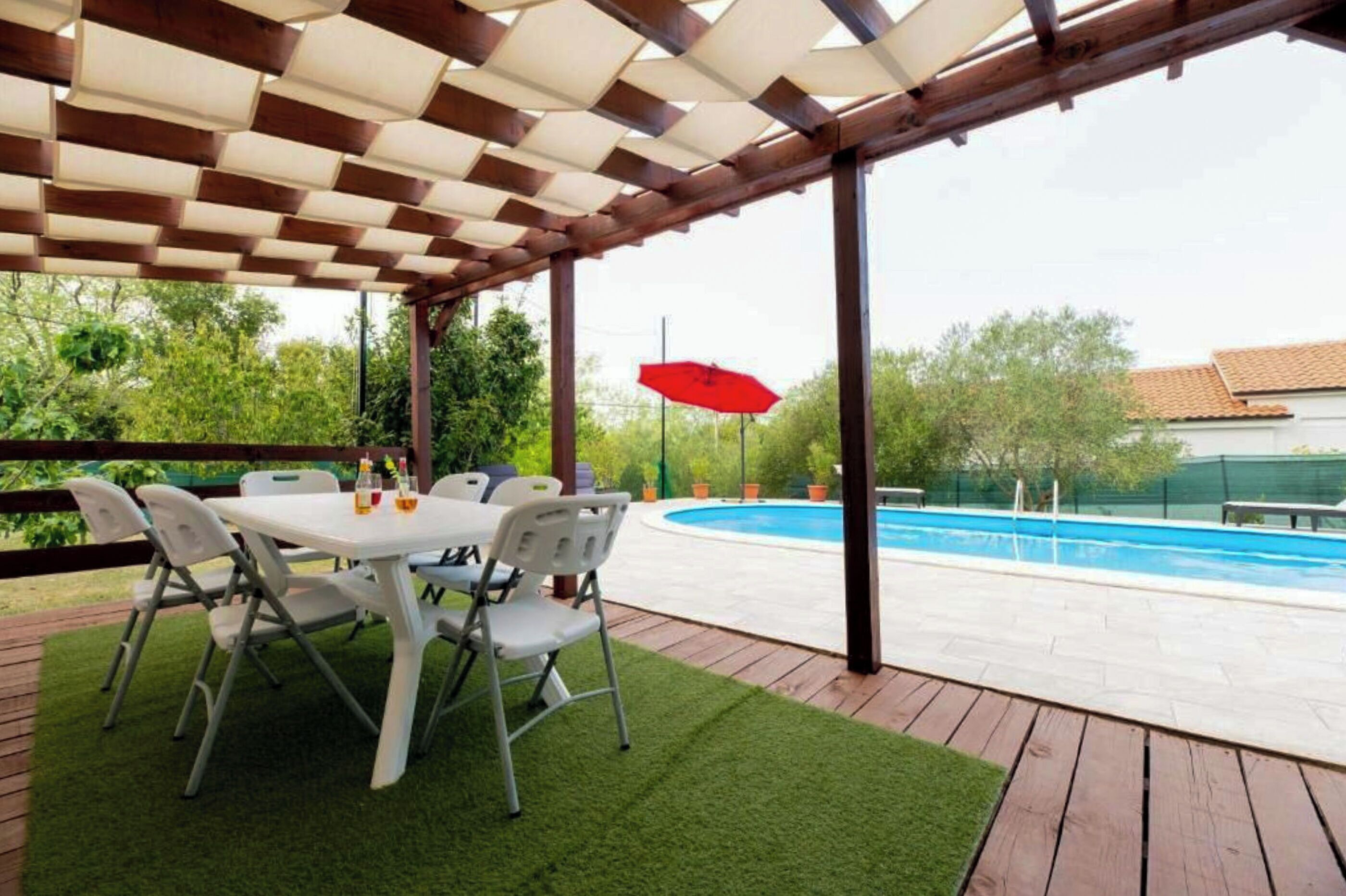 Un espace extérieur abrité comprenant une piscine, une table avec des chaises et un parasol rouge.