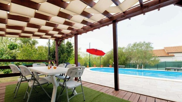 A covered outdoor area with a pool, a table with chairs, and a red umbrella. - House Bistre With Private Pool (Razanac)