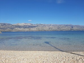Ein klarer See mit kiesigem Ufer und fernen Bergen.