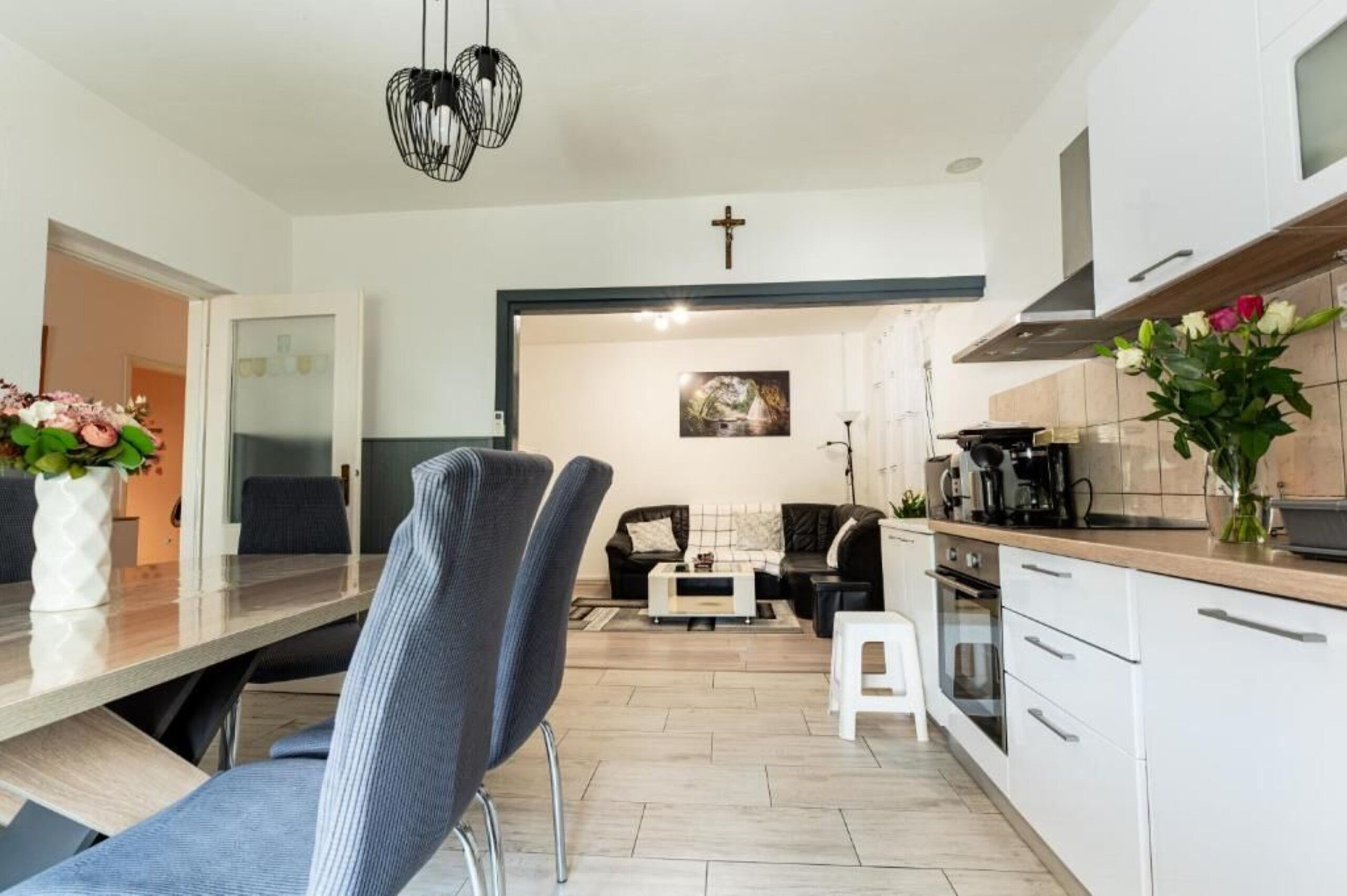 A modern kitchen with white cabinets, a dining area with a table and chairs, and a living room with a sofa and coffee table.