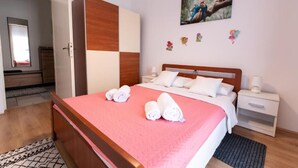 A neatly made bed with a pink bedspread and white pillows, a wooden wardrobe, a bedside table with a lamp, and a painting on the wall. - House Bistre With Private Pool (Razanac)