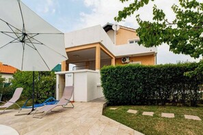 Ein modernes Haus mit einer Terrassenfläche, einem weißen Sonnenschirm und einem gepflegten Heckenstreifen.