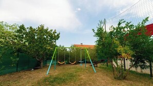 A fenced backyard with a swing set, trees, and a building in the background. - House Bistre With Private Pool (Razanac)
