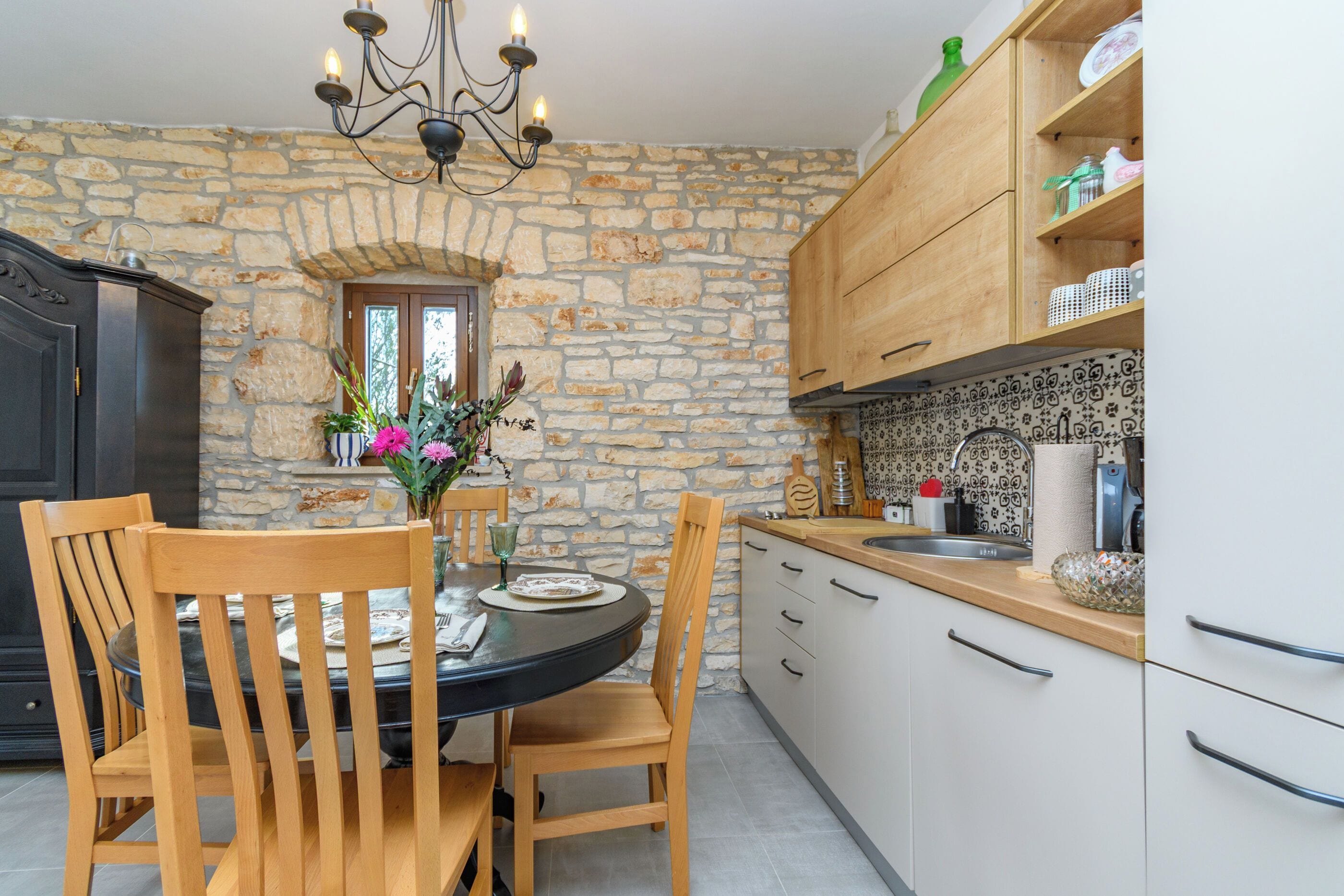 A kitchen with stone walls, wooden cabinets, a dining table with chairs, and a chandelier.