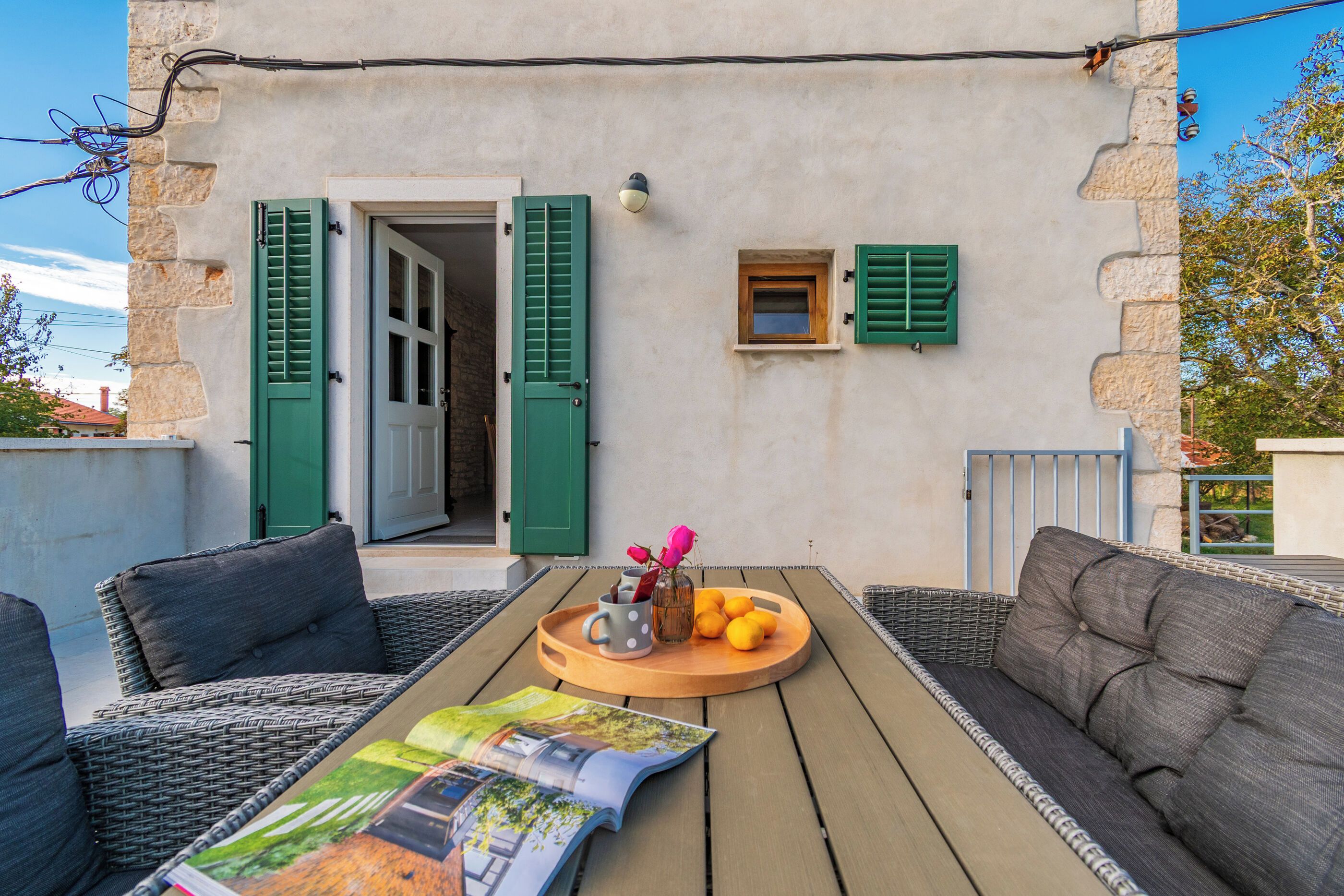 Un espacio al aire libre con mobiliario de mimbre, una mesa de madera con una revista y una ventana pequeña con persianas.