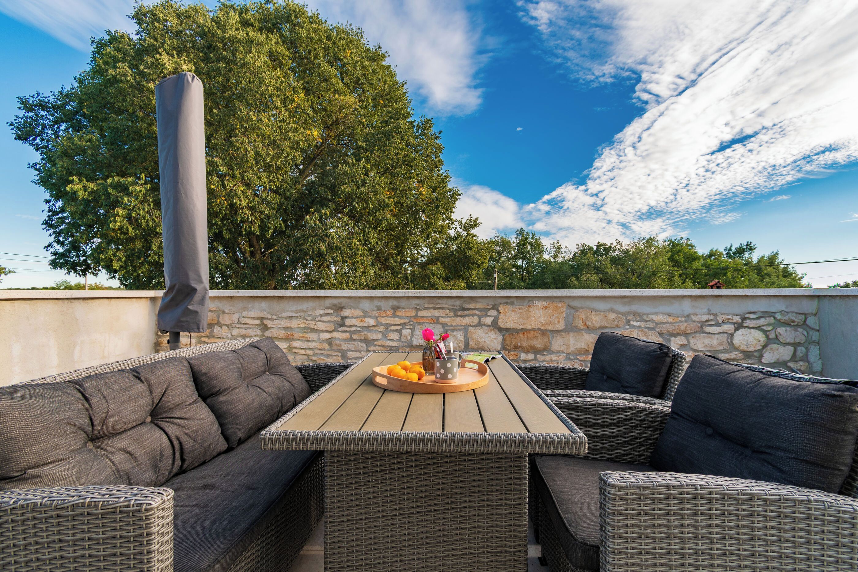Eine Terrasse im Freien mit Korbmöbeln, einem Tisch mit Obstschale und einer Steinmauer.