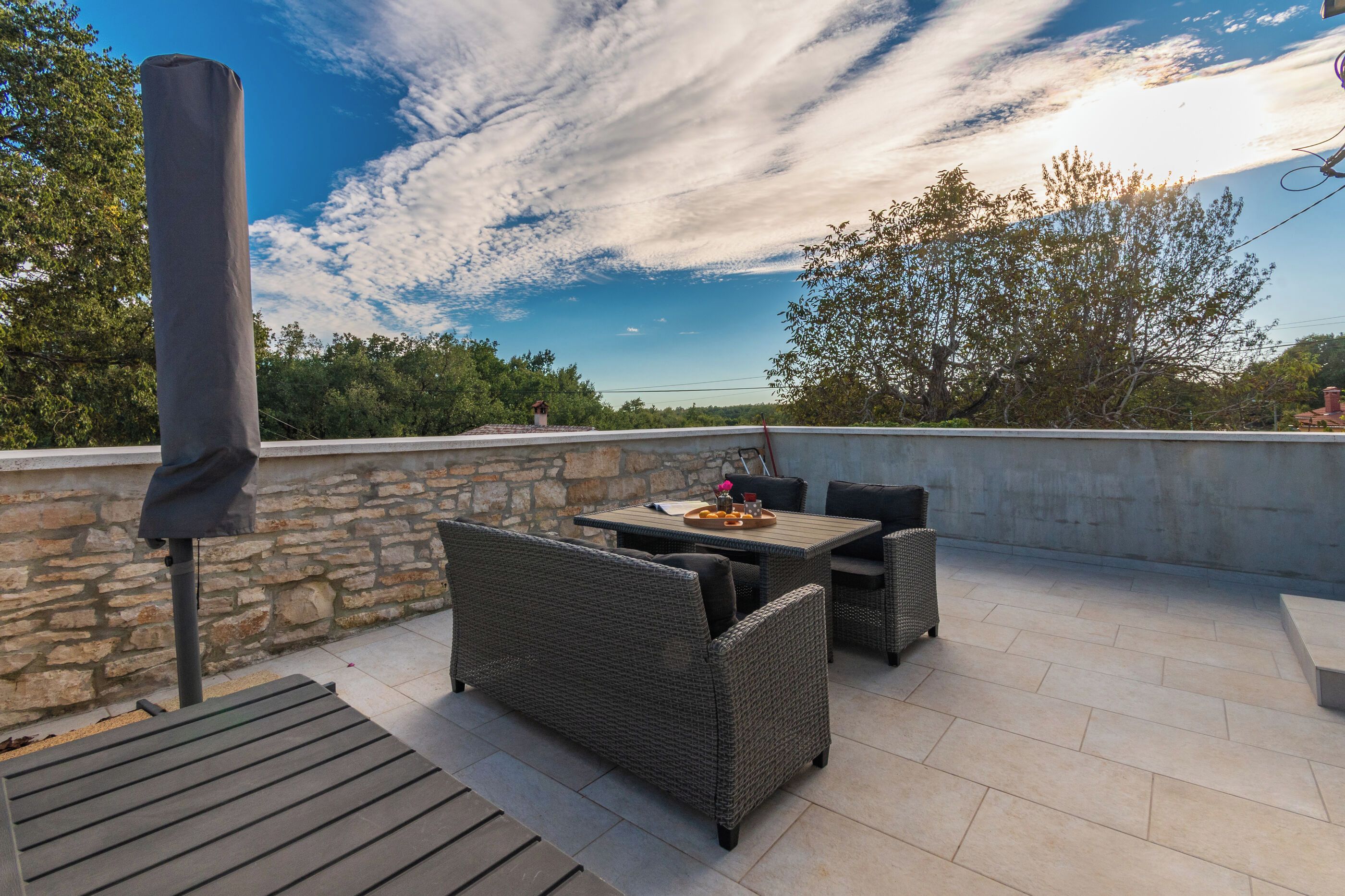 An outdoor patio with wicker furniture, a stone wall, and a view of trees and sky.