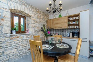 Un espace repas avec un mur en pierre, des chaises en bois, une table noire et un lustre.
