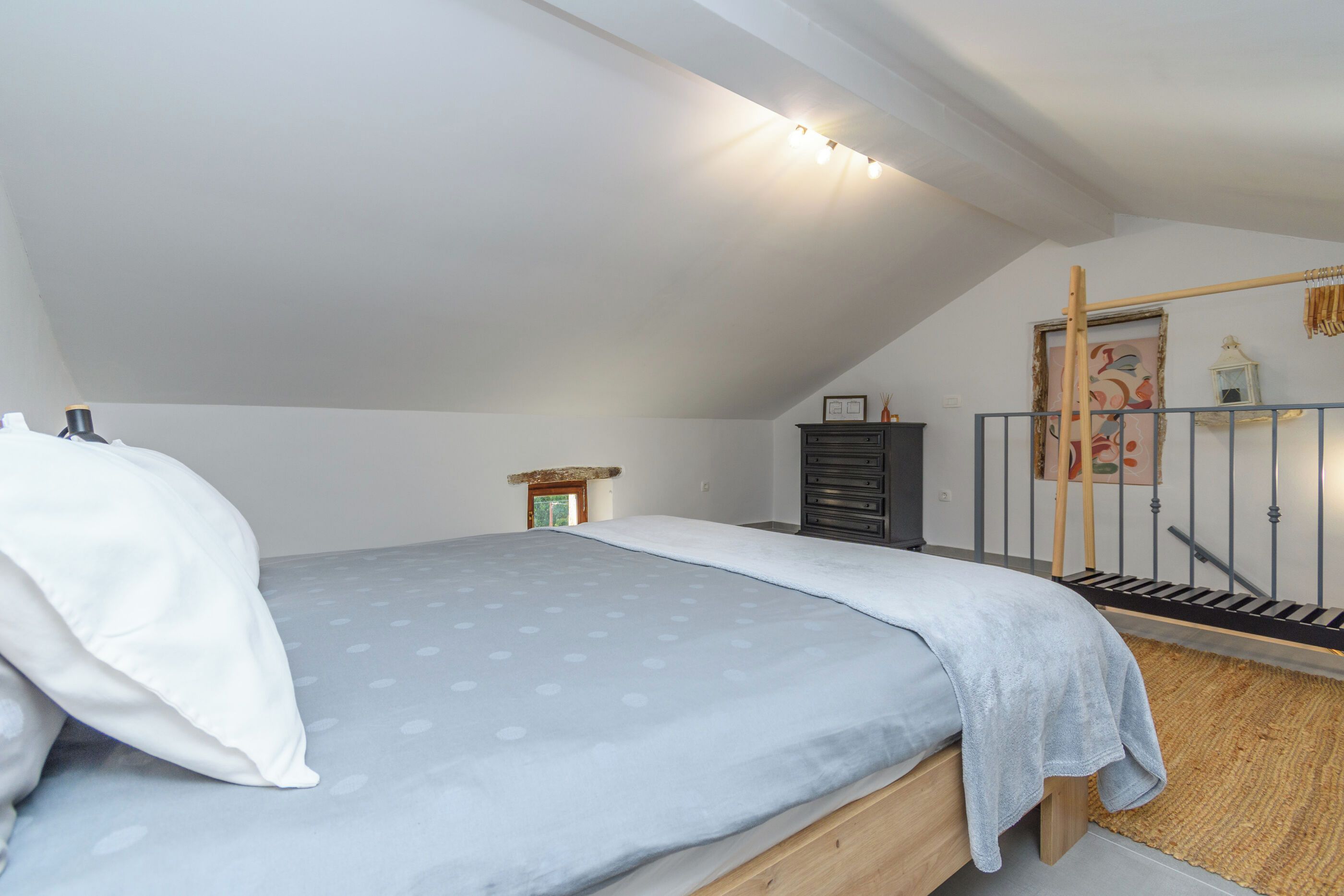 A bedroom with a bed, a dresser, a ladder, and a painting on the wall.