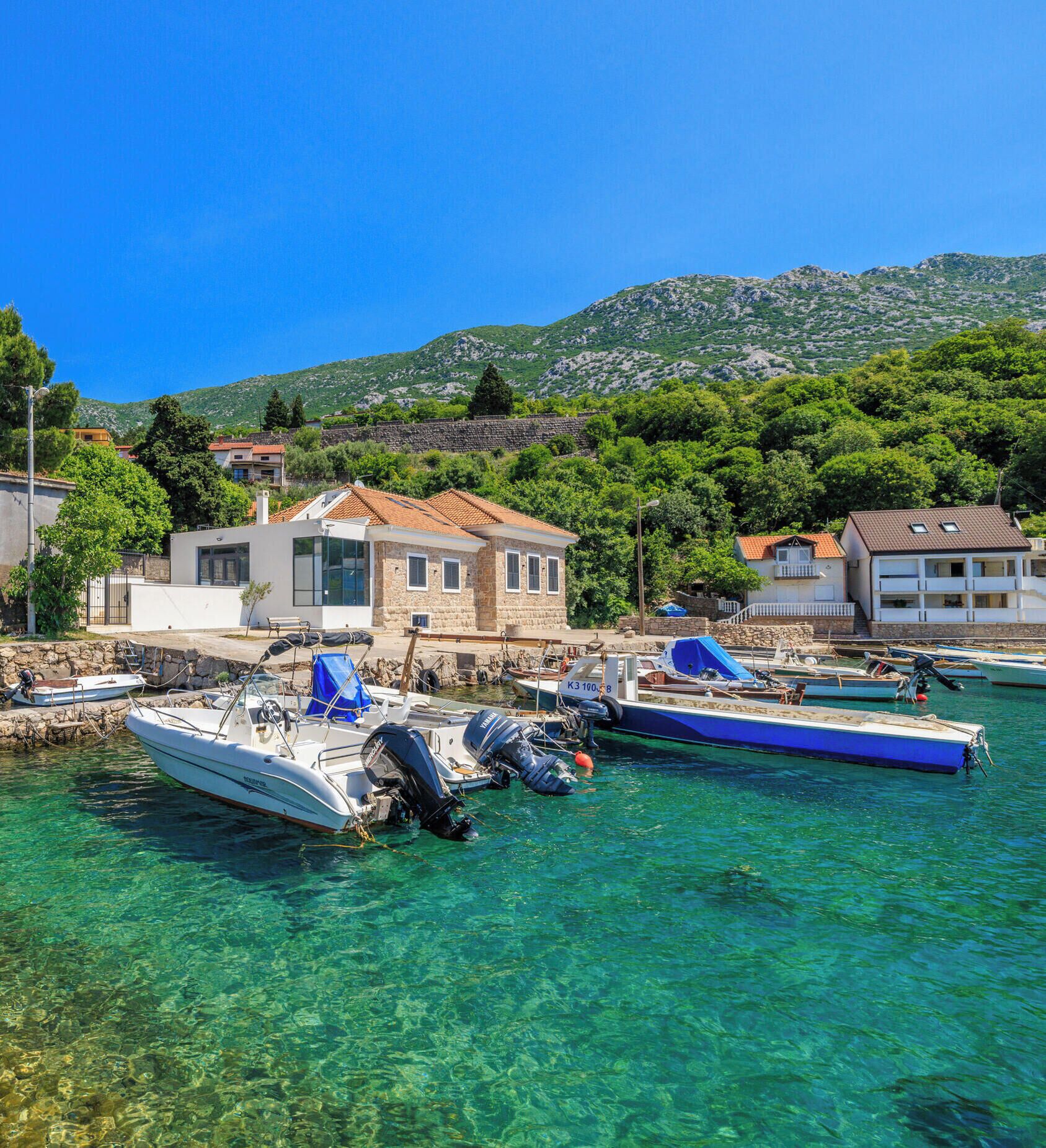 A coastal village with clear waters, boats docked, and traditional stone buildings.