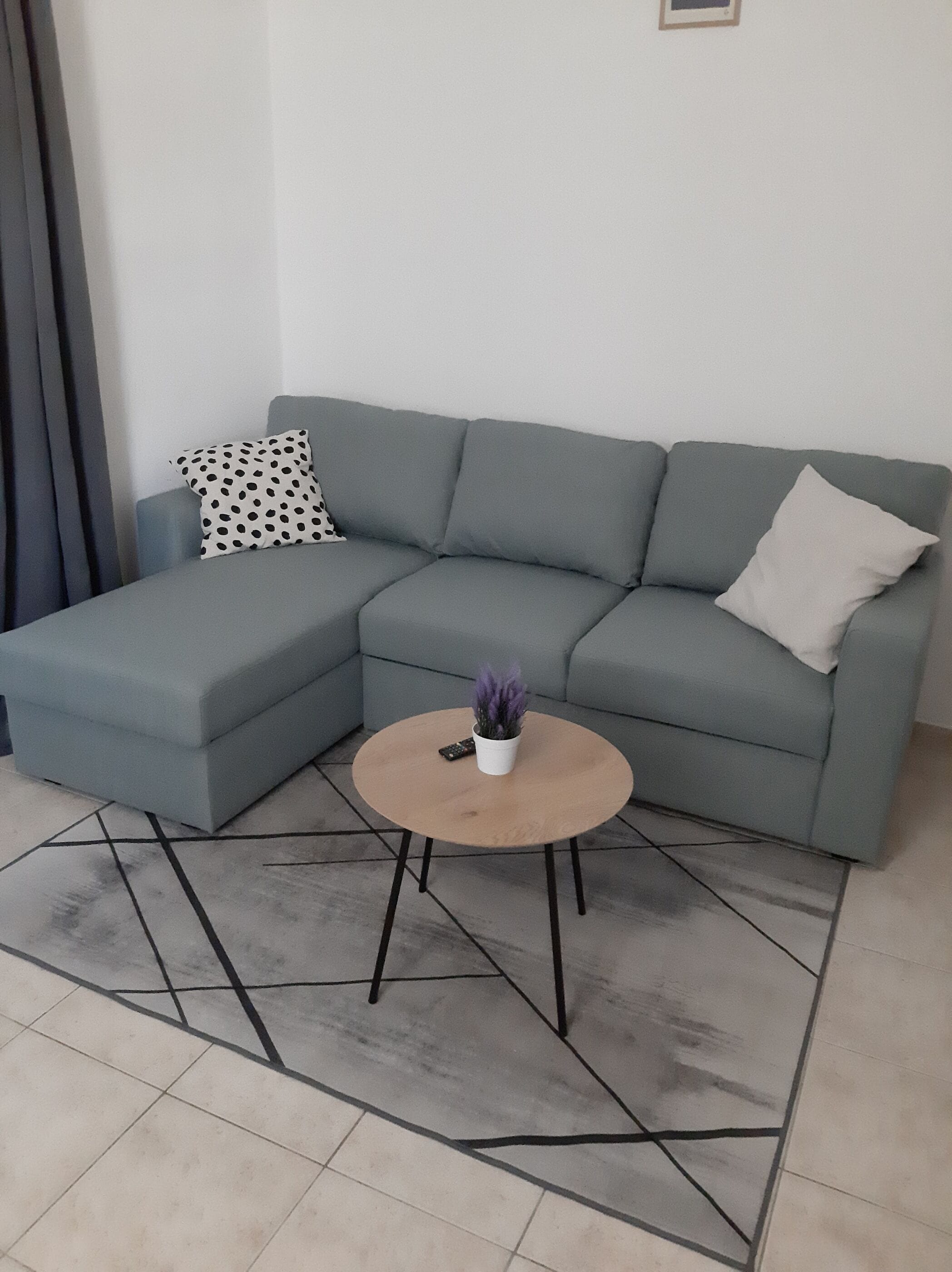 Ein modernes Wohnzimmer mit einem grauen Ecksofa, einem runden Couchtisch aus Holz und einem kleinen Topfpflanzen.