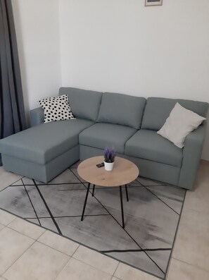 A modern living room with a grey sectional sofa, a round wooden coffee table, and a small potted plant. - House House Marijan (Karlobag)