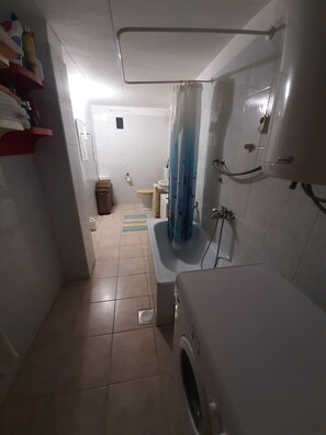 Pieni kylpyhuone, jossa on pesukone, wc ja suihkutila.