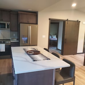 A modern kitchen with a central island, stainless steel appliances, and a sliding door leading to a bedroom. - Newly Constructed 2 bedroom, 1 bath home, quiet, private. (Shelton)