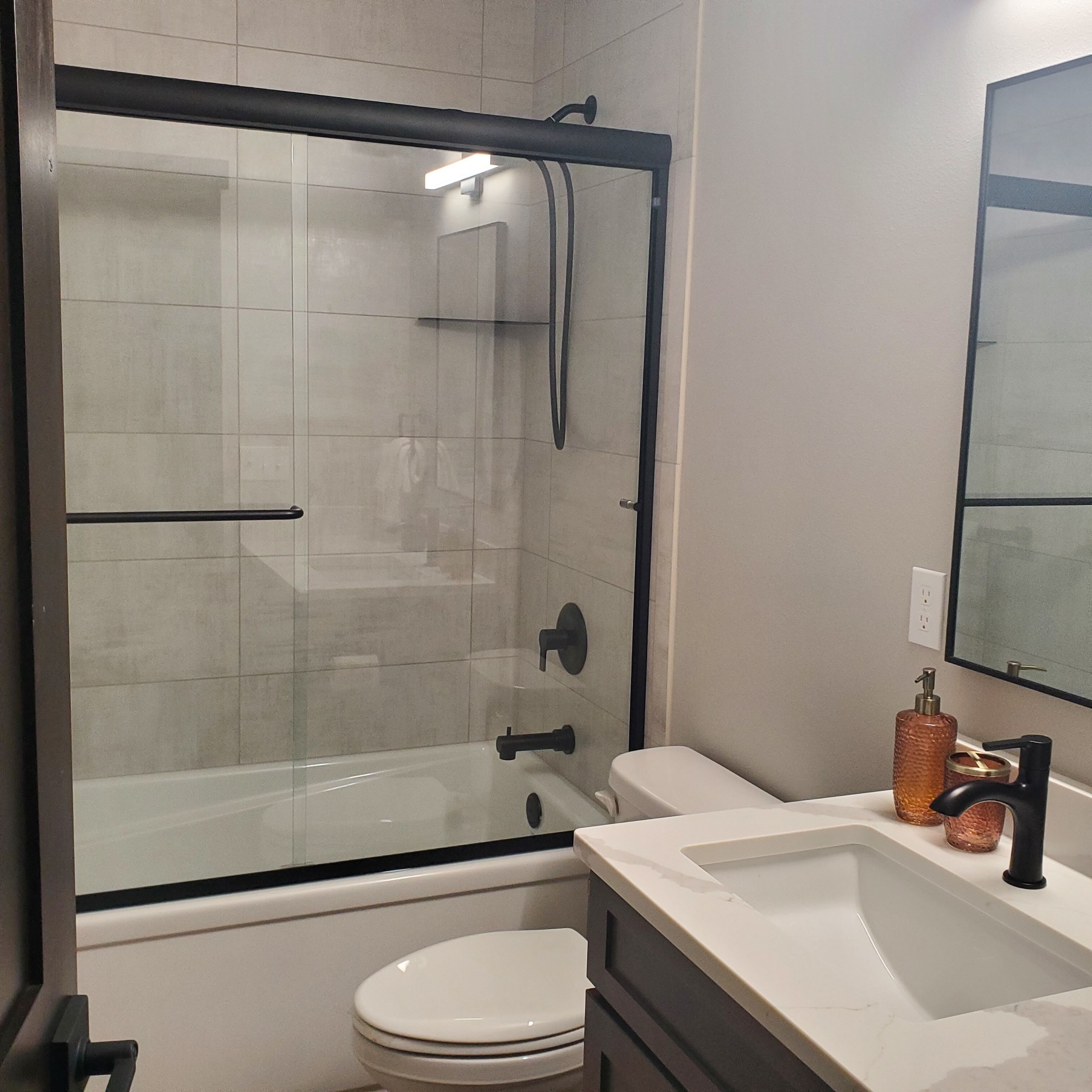 Un bany amb dutxa d'envidriat, vàter blanc i un lavabo amb mirall a la part superior.