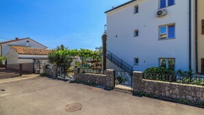 Un edificio de dos pisos con un muro de piedra, una reja metálica y una escalera que lleva a la entrada.