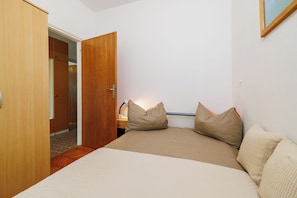 Un dormitorio con cama, almohadas, una mesita de noche, un armario de madera y una puerta a otra habitación.