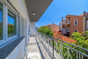 Un balcón con barandilla de metal, una silla blanca y vistas a edificios vecinos.