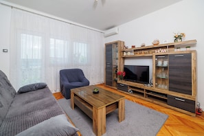 Una sala de estar con sofá, una mesa de centro, un mueble de televisión con estantes y un ventanal con cortinas.