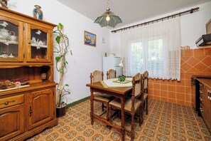 A dining area with a wooden table, chairs, a cabinet with glass doors, a potted plant, and a window with a curtain. - Apartments Smiljka (Crikvenica)
