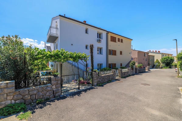 Un edificio residencial con un muro de piedra, una reja metálica y un cielo despejado.