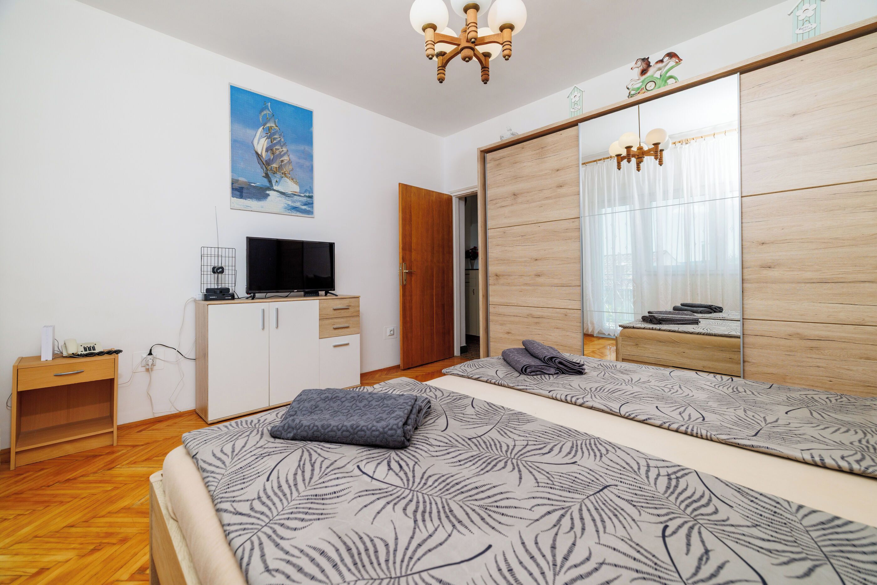 A bedroom with two beds, a TV, a wardrobe, and a painting on the wall.
