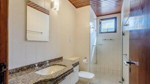 A bathroom with a granite countertop sink, a toilet, a glass-enclosed shower, and a wooden ceiling.