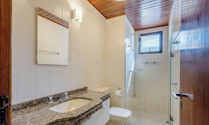 Une salle de bain avec un lavabo sur un comptoir en granit, des toilettes et une douche à parois de verre.