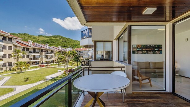 A balcony with a table and chairs, overlooking a residential area with multiple buildings and a green hill in the background.