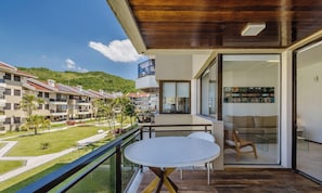 Un balcon moderne avec une table ronde et des chaises, donnant sur un espace paysager et offrant une vue sur d’autres bâtiments et des collines.