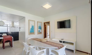 Un salon moderne avec un coin repas, un téléviseur à écran plat fixé au mur et une cuisine visible au fond.