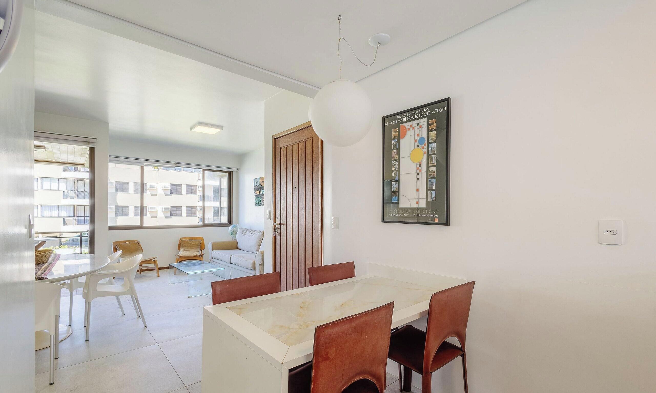 A modern dining area with a marble table and brown chairs, a large window with a view of buildings, and a framed artwork on the wall.