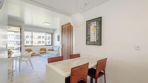 A modern dining area with a marble table and brown chairs, a large window with a view of buildings, and a framed artwork on the wall.