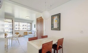 A modern dining area with a marble table and brown chairs, a large window with a view of buildings, and a framed artwork on the wall. - Charm and Elegance by the Sea! Rit0201 (Florianópolis)