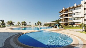 Een resort met een groot zwembad, ligbedden en een meerlaags gebouw met balkons.