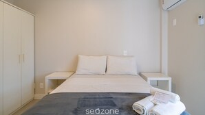 Een hotelkamer met een bed, nachtkastje, kledingkast en een airconditioner.