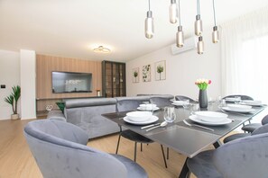 Ein modernes Wohnzimmer mit Essbereich, grauen Sofas, einem Flachbildfernseher und einem Esstisch für vier Personen.