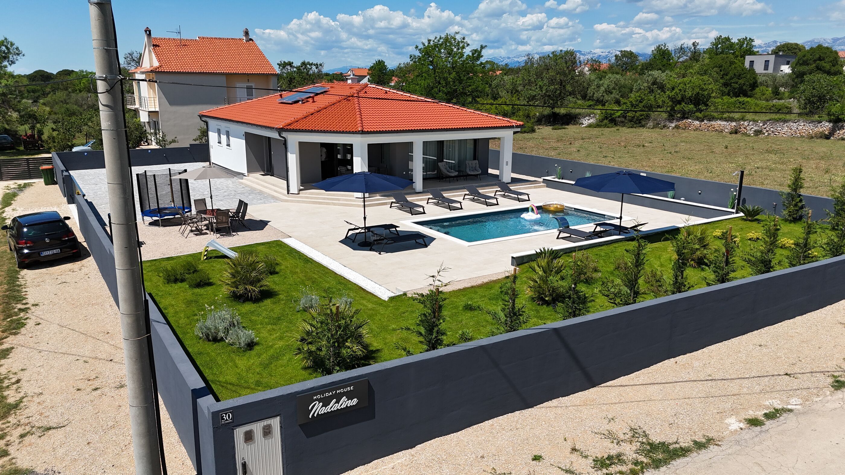 A modern holiday house with a swimming pool, outdoor seating, and a view of mountains.
