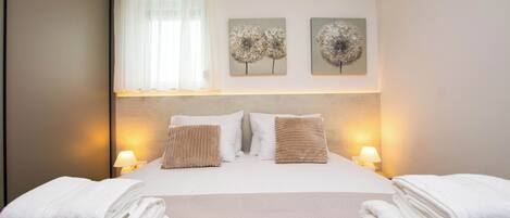 A hotel room with a bed, two wall-mounted lamps, a window with sheer curtains, and two wall art pieces.