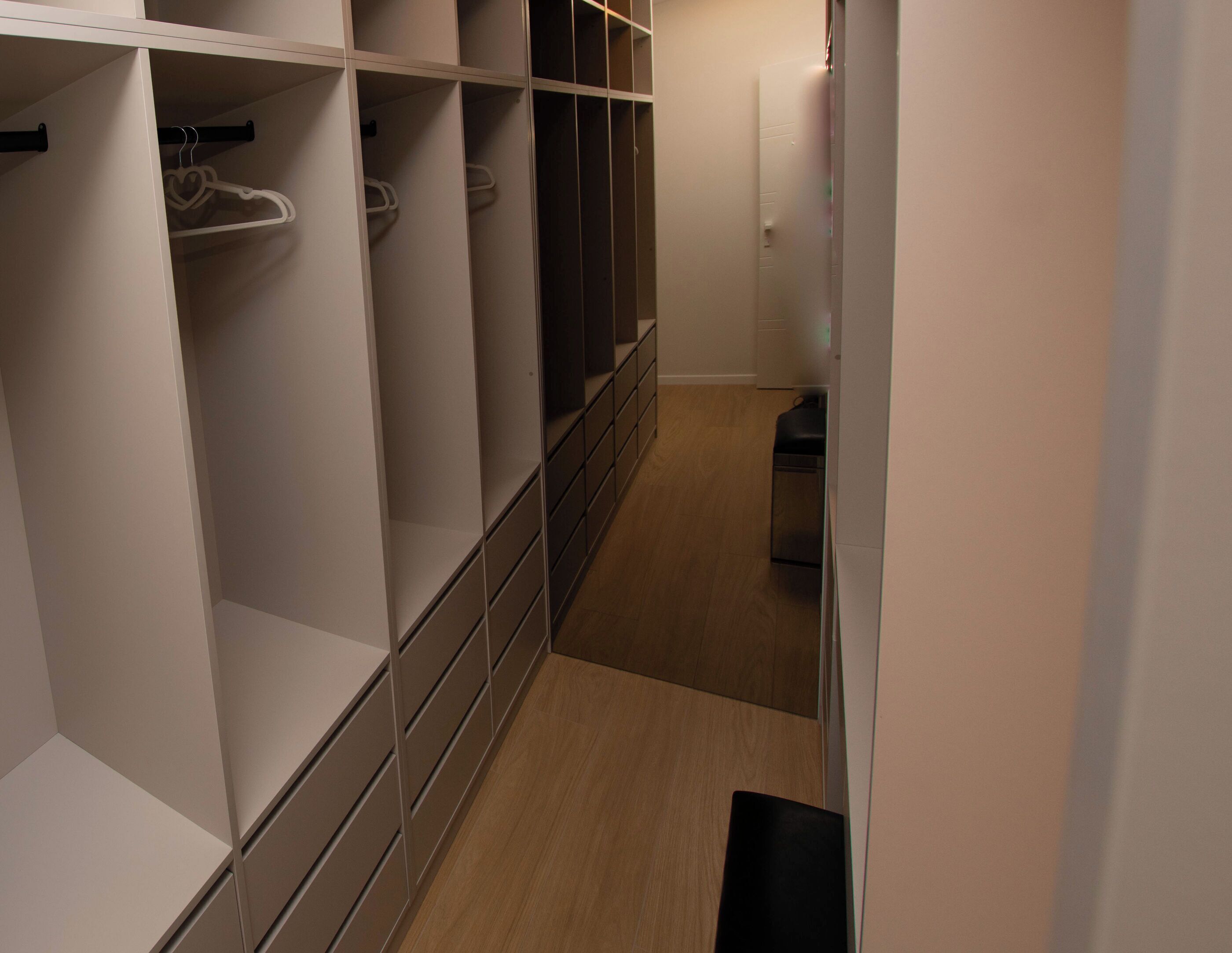 Ein schmaler Flur mit Holzboden, einem weißen Schrank mit Regalen und Kleiderstange sowie einer schwarzen Mülltonne.
