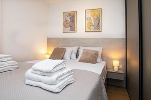 Ein ordentlich bezogenes Bett mit gefalteten Handtüchern, einem Kopfteil und zwei an der Wand befestigten Kunstwerken.