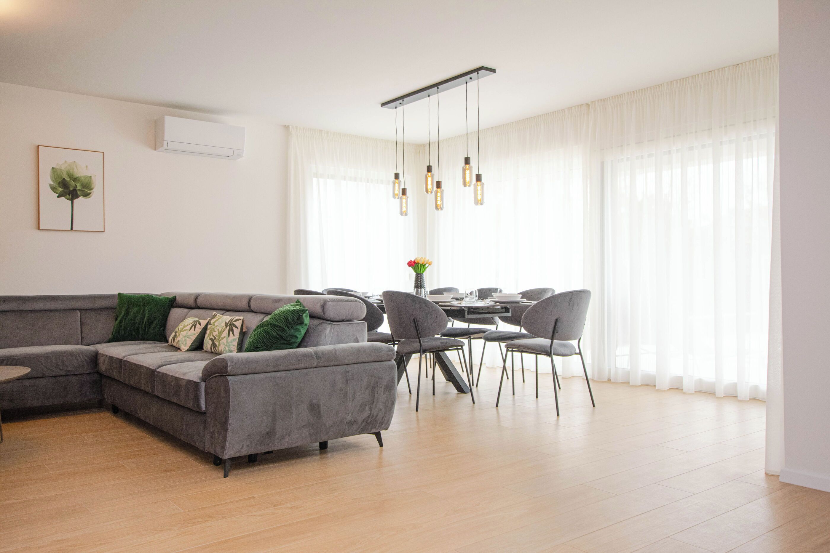 Una sala de estar moderna con un sofá gris, una mesa de comedor con sillas y una lámpara colgante.