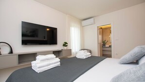 A modern hotel room with a large bed, a flat-screen TV mounted on the wall, a small plant, and a neatly made bed with folded towels. - House Nadalina (Vrsi)