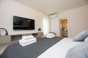 Ein modernes Hotelzimmer mit einem großen Bett, einem flachbildfernseher an der Wand, einer kleinen Pflanze und einem ordentlich bezogenen Bett mit gefalteten Handtüchern.