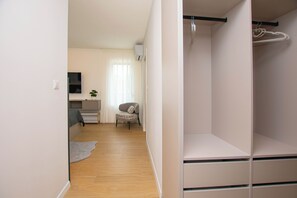 Ein Zimmer mit einem Bett, einem Schreibtisch, einem Stuhl und einem Kleiderschrank mit Kleiderstange.