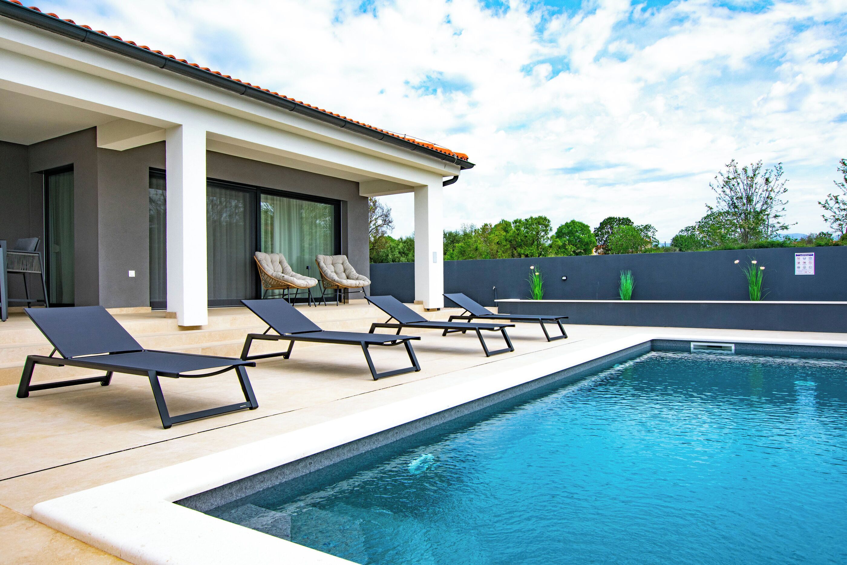 A swimming pool with lounge chairs, a covered patio, and a view of the surrounding greenery.