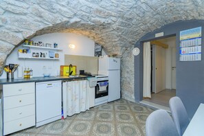 A compact kitchen with a stone arch, white cabinetry, a dishwasher, a stove, and a calendar on the wall. - Apartment D and D (Punat)