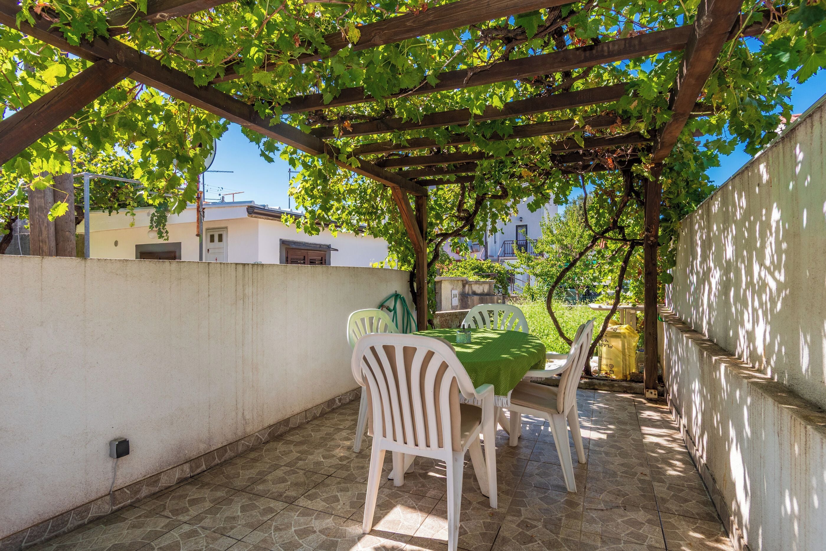 Eine Außenpatio mit einer Pergola, einem Tisch mit Stühlen und Blick auf Gebäude im Hintergrund.