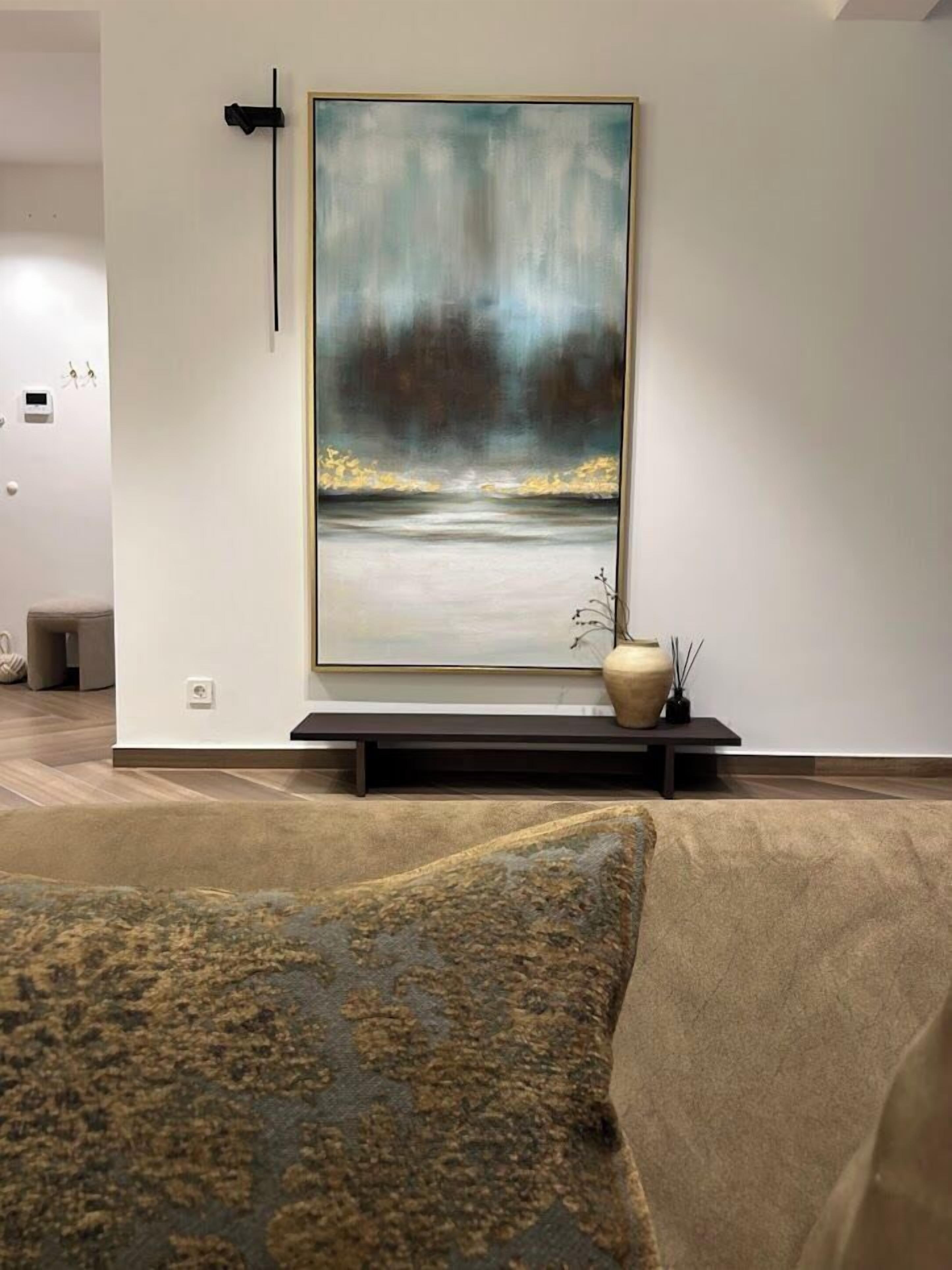 Una sala de estar moderna con un cuadro abstracto grande, un sofá y una pequeña mesa con un florero.