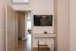 Un pasillo con puerta de madera, televisor montado, repisa con un florero y un banco con toalla.